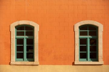 Two green timber framed windows aginst a bright orange toned exterior wall