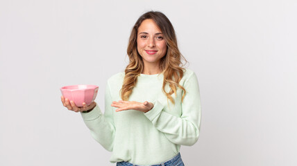 pretty thin woman smiling cheerfully, feeling happy and showing a concept and holding an empty pot bowl - obrazy, fototapety, plakaty