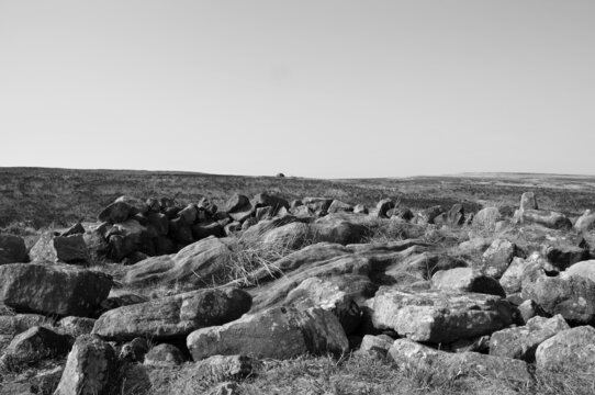 monochrome image of the exposed stones at the top of a cairn known as the millers grave on midgley moor in calderdale west yorkshire with pennine moorland scenery