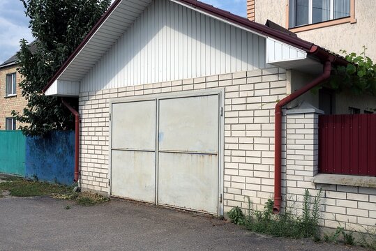 white brick facade of the garage with gray metal gates and part of the fence on the street by asphalt road