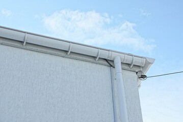 white plastic gutter pipes on the gray wall of the building on the street against the background of the sky