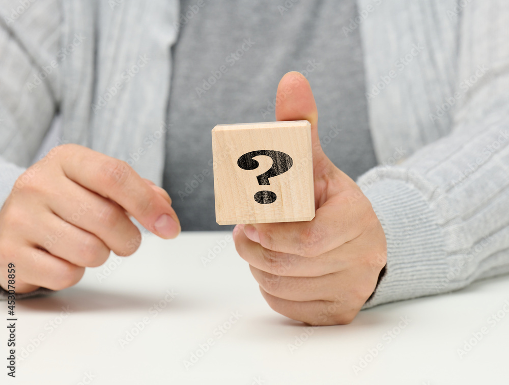 Poster female hand holding a wooden cube with a question mark, concept of answers and questions, suspense a