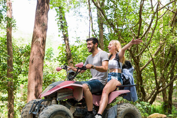 Young man and woman driving off road adventure with happy and smiling. Couple riding on ATV bike or quad bike on road along forest trail on mountain. Camping, jungle adventure concept © amorn