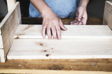 A carpenter measures the planks to assemble the parts, and build a wooden table for the customer.