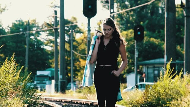 Young beautiful woman walks alone on the railway tracks. Slow Motion. Front view of a lonely slender pretty girl walking away into the distance. Sunny summer day. 4K.