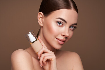 Portrait beautiful young woman with clean fresh skin. Model with foundation makeup bottle....