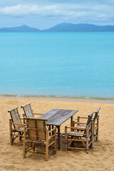 Fototapeta na wymiar Wooden bamboo furniture, table and five chairs around on sand beach with blue sea water background in Koh Samui island, Thailand