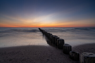 long exposure of an ocean sunset with sandy beach and wooden pylon storm groin in the foreground