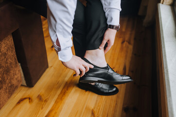 Fototapeta premium A stylish man businessman in a white shirt puts on black shiny shoes on his feet, going to work in the morning. Business photography.