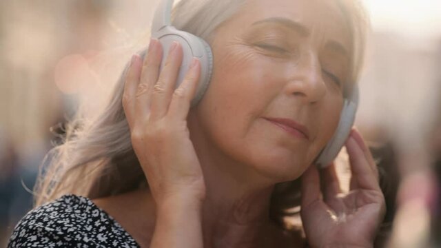 Portrait of joyful senior grey hair woman listening to music in headphones. Closeup face of beautiful middle age lady with long hair. Portrait of gorgeous woman. 