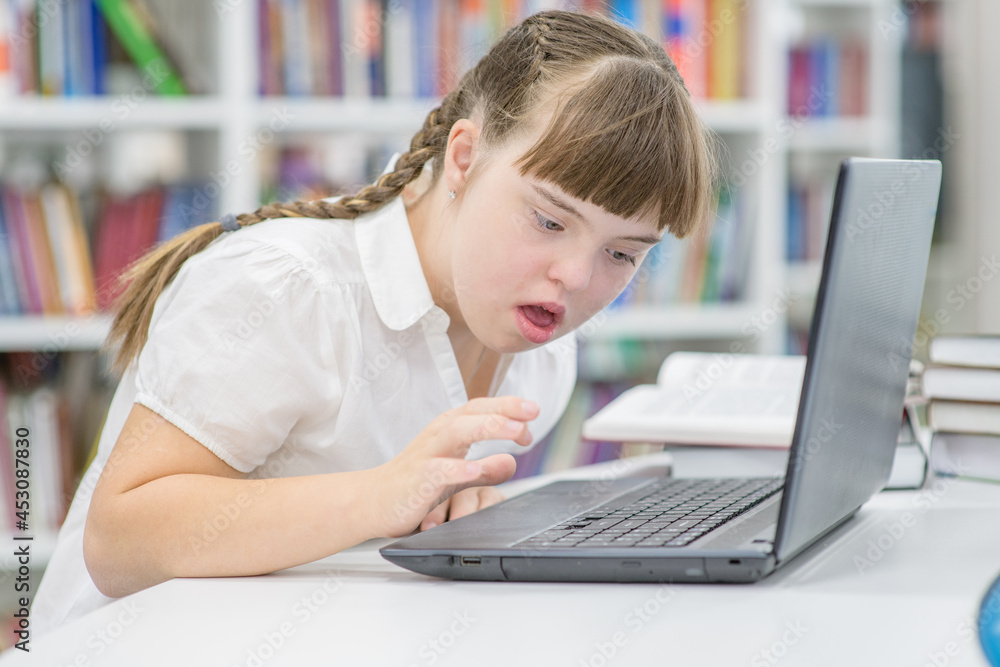 Wall mural girl with syndrome down uses a laptop at school. education for disabled children concept