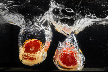 Fresh two parts orange, slices falling into the water with a splash of water and air bubbles, isolated on a black background.