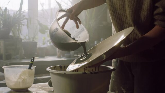 Woman ceramist is pouring glaze on big plate, glazing it manually, rotating the plate to spread liquid evenly, ceramics art, Foreground, Slow motion.
