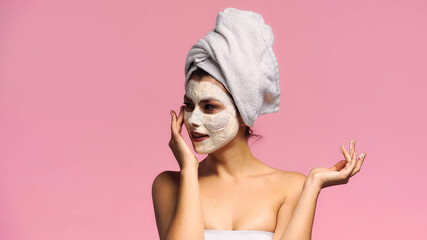 young woman applying clay mask on face while looking away isolated on pink