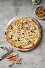 Tasty pizza with  sausage, mozzarella, marinated mushrooms, black olives, green onion on marble round tray. Garnished on grey stone backdrop with pizza ingredients