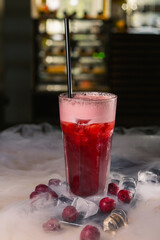 Refreshing cold cherry cocktail with straw placed on table with frozen berries and steam in dark bar 