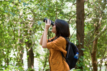 Portrait of Asian young woman hiker hiking with backpack standing holding binoculars looking for birds along forest trail