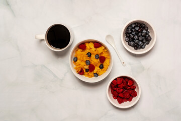 Continental breakfast of coffee, cornflakes cereal, raspberry and blueberry on a white marble surface