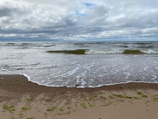tide of the sea on the sandy shore against the background of blue sky and white clouds in the summer season.