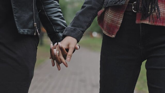 Close up shot with tracking of young female couple holding hands and walking in park on date