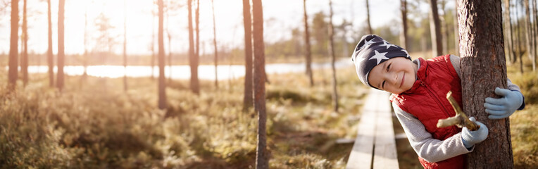 Cute boy in the forest hugging a tree's trunk