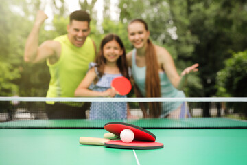 Family near ping pong table in park, focus on rackets and ball
