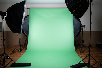 Front view of a green screen cloth backdrop with four photography LED softbox lights on tripods illuminate to the backdrop, get ready for take a shoot, making a video or broadcast TV in the studio.