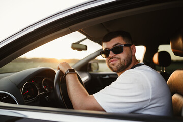 Naklejka premium Bearded man driver in sunglasses sitting in his car and looking at camera
