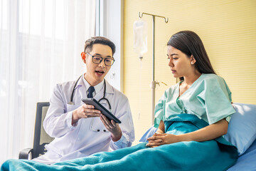 Asian male doctor talking to asian female patient in bed, while explaining exam results in computer to patient at medical consultation, Medicine and health care concept, selective focus point.