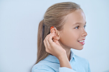 Profile of girl touching ear with hearing aid