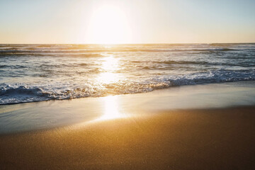 waves breaking on the shore of the beach with foam at sunset