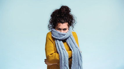 frozen woman hiding face in warm scarf isolated on blue