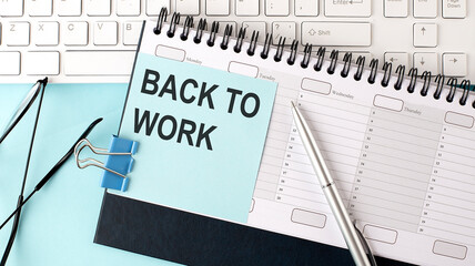BACK TO WORK text on blue sticker on planning and keyboard,blue background
