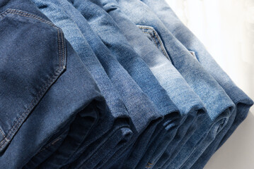 a pile of blue jeans on a light background. Close up. Sunlight. Diagonal