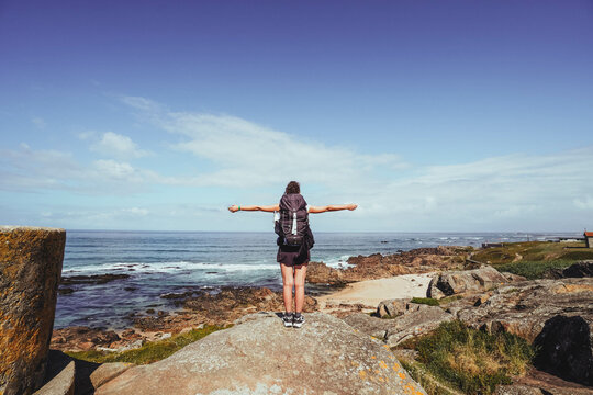 pilgrim woman with open arms on top of a rock looking at the horizon