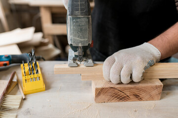 Joinery work. Close up of hand carpenter working on wood with electric jigsaw in workshop. Sawing...