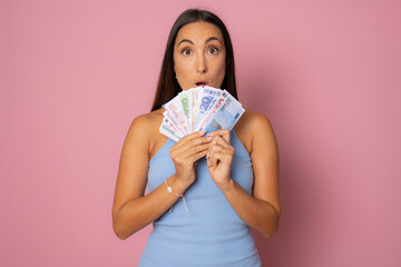 Image of young funny woman standing over pink wall wearing hat holding money.