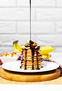 Pancakes with Chocolate Syrup, Nuts and Bananas. Stack of whole flapjack. Chocolate Being Poured Into Slapjack, Tasty breakfast and Healthy Food