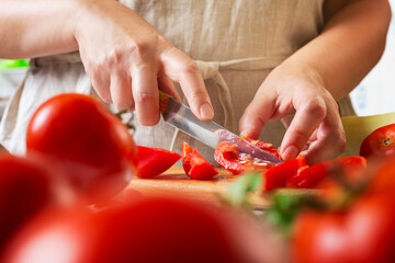 Chef slicing tomato using knife on the table in restaurant. Process of cutting and preparation food...