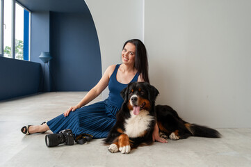 A girl in a blue dress with Berner Sennenhund in an embrace lies on the floor