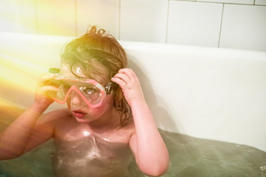 Girl wearing snorkel goggles in bathtub