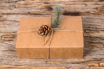 Craft gift box with fir branch and pine cone on old wooden background. Eco friendly holiday concept.
