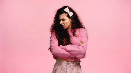 offended woman turning away while standing with crossed arms isolated on pink