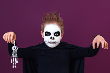 Little boy in halloween costume holds skeleton and scares the camera on purple background.