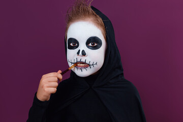 Child with Halloween makeup in skeleton costume eats Halloween jelly worms.