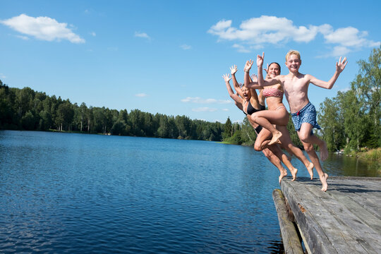 Young friends jumping into lake - Powered by Adobe