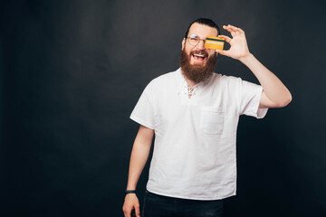 Naklejka premium Excited bearded man is covering one eye with a credit card.