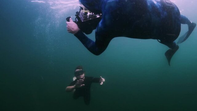 Underwater photography with model. Woman swims underwater with professional camera housing in the freshwater lake and takes pictures of the male model
