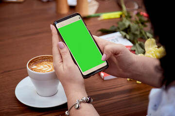 Chroma key mobile phone screen in woman's hand and cup of coffee on the table. Top view. Education,...