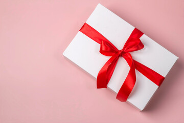 White gift box with satin red ribbon bow on peach background with copy space